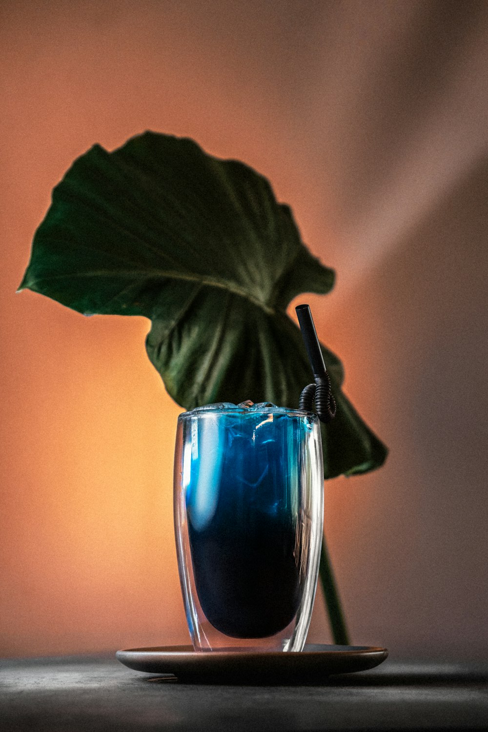 a glass with a blue liquid and a green leaf