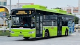A green and black electric city bus with signage indicating it is on route 3 to Punggol Field/Central. The bus displays markings suggesting it is an eco-friendly electric bus operated by SBS Transit. It is stationed at a bus interchange area with buildings and road signs in the background.