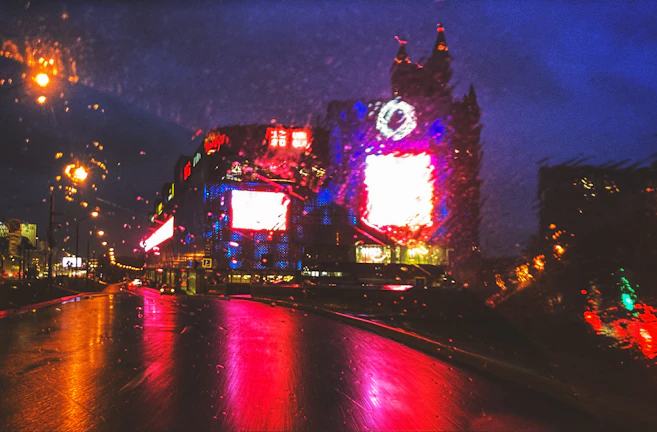 Vibrant city street scene with colorful lights reflecting on wet pavement.