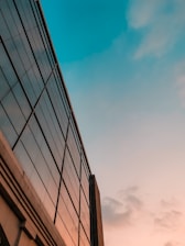 Modern office building with glass facade reflecting the sky during sunset.