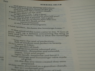 A close-up of a Bible page showing text from Ezekiel 28:8-14. The text includes references to a shining splendor, a violent death, and descriptions of Eden with precious stones.