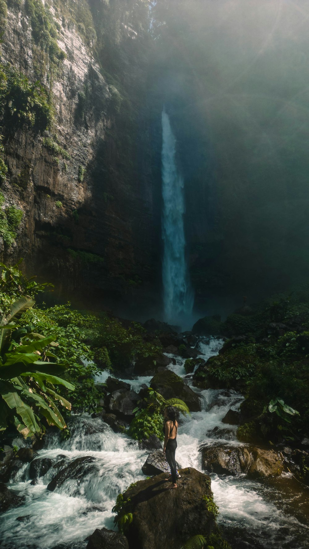 a person standing on a rock in front of a waterfall