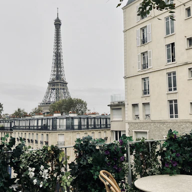 A cozy Parisian apartment balcony with flowers and a view of the Eiffel Tower at sunset.