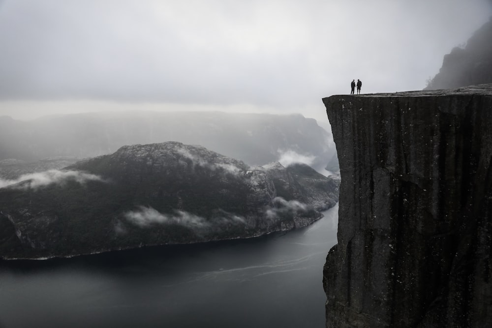 two people standing on a cliff overlooking a body of water