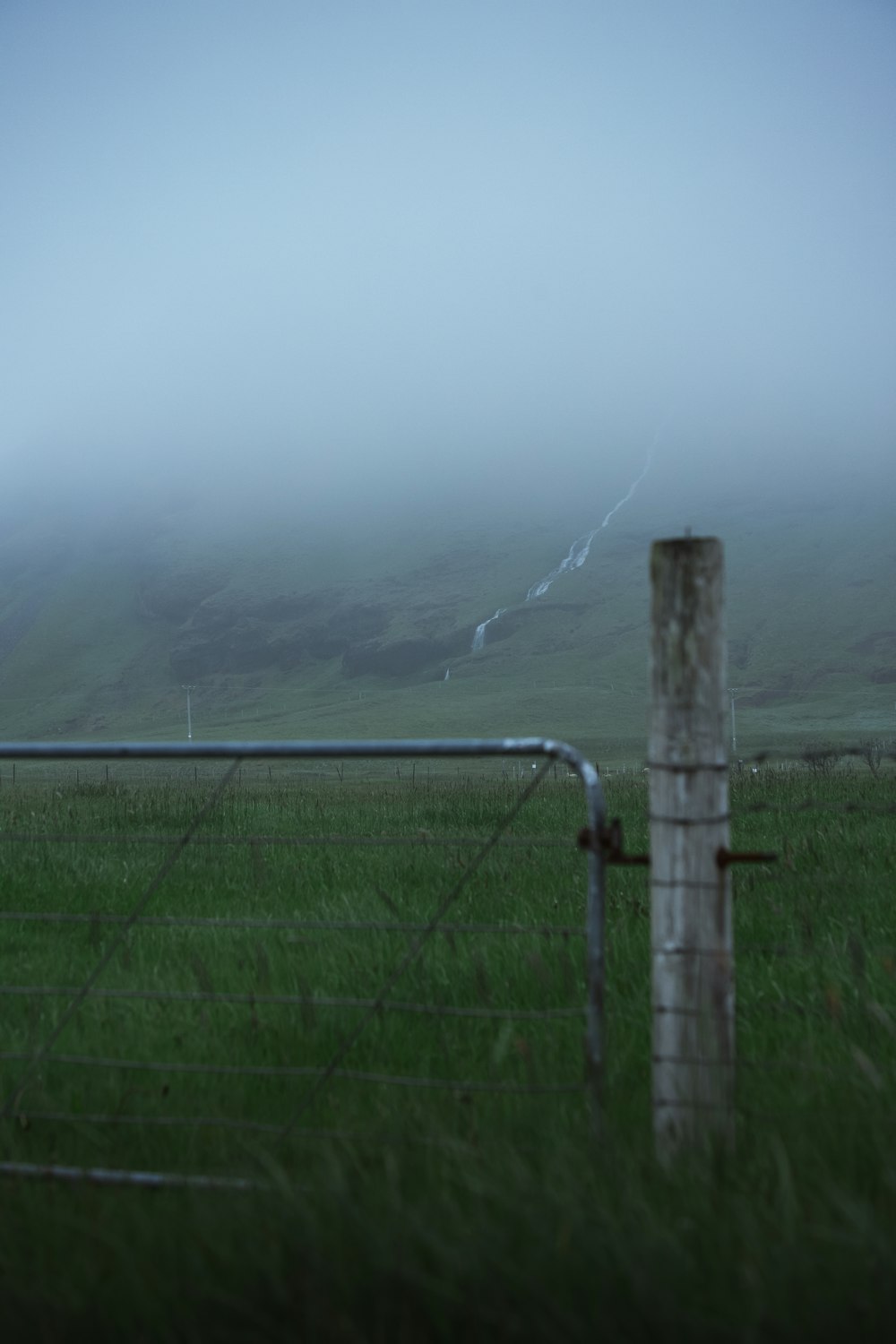 a fence in a grassy field with a mountain in the background