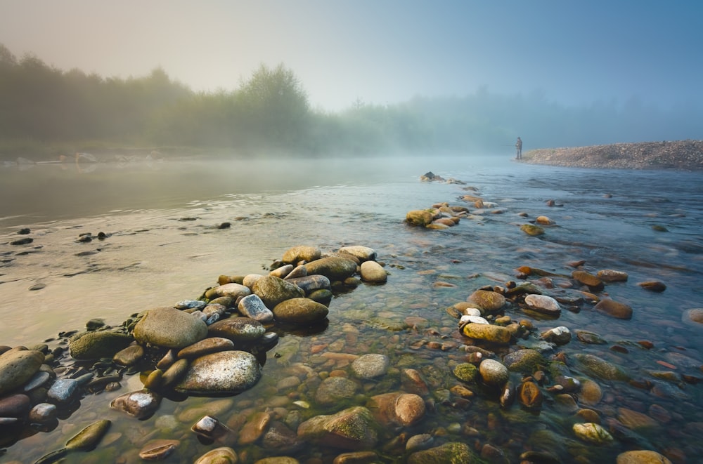 a river with rocks in the water and a person standing in the distance