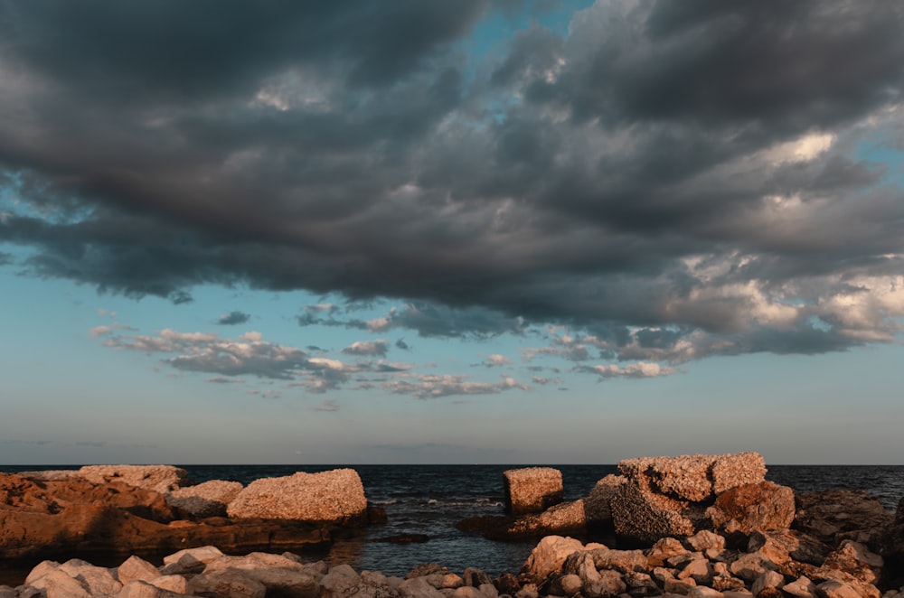 a cloudy sky over the ocean with rocks in the foreground
