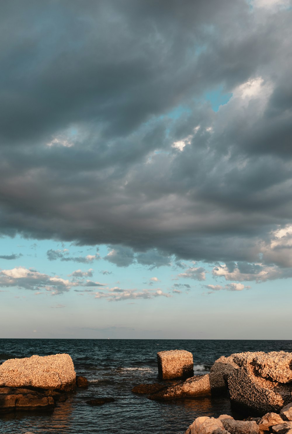 a person standing on rocks near the ocean under a cloudy sky