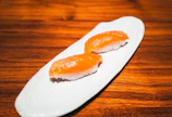 Fresh salmon nigiri sushi arranged on a sleek black plate under soft neon lighting.