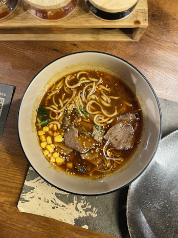 A colorful bowl of ramen noodles topped with tender beef slices and fresh vegetables.