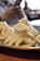 Steamed dumplings with intricate folds displayed on a metal plate. The background reveals a person holding a phone, slightly out of focus, in a dining setting.