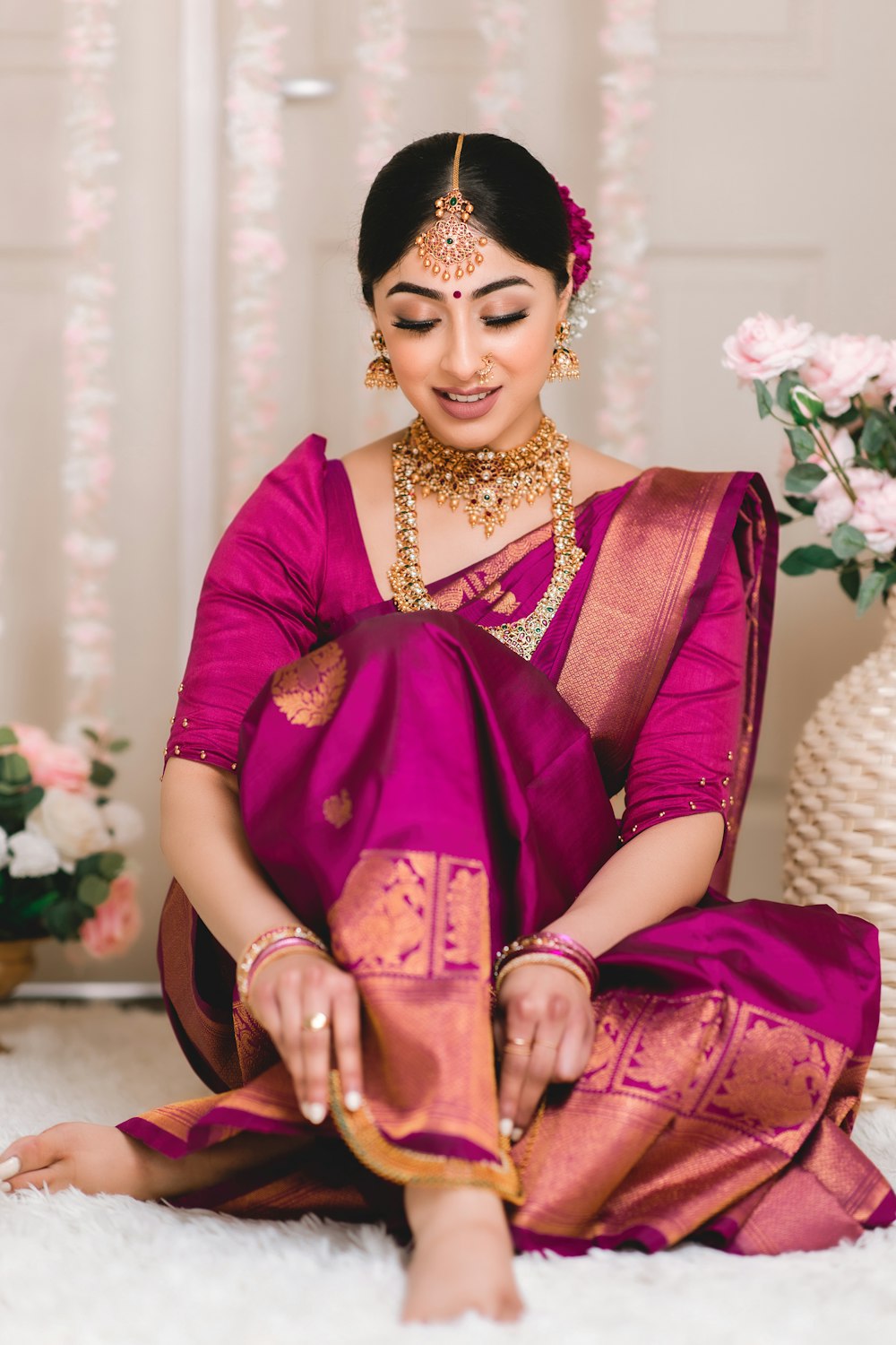 a woman in a pink sari sitting on a white rug