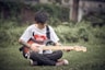 a young man sitting in the grass playing a guitar