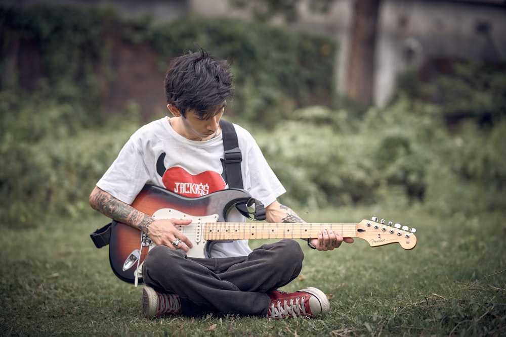 a young man sitting in the grass playing a guitar