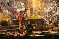 A vibrant scene depicting a traditional ceremony with a priest holding ritual items, surrounded by an appreciative crowd. The atmosphere is filled with smoke and warm lighting, creating a spiritual and festive ambiance.