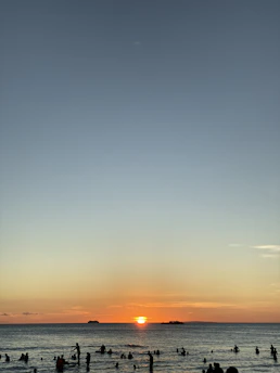Vibrant orange sunset over Cabo San Lucas bay with swimmers silhouetted in water.