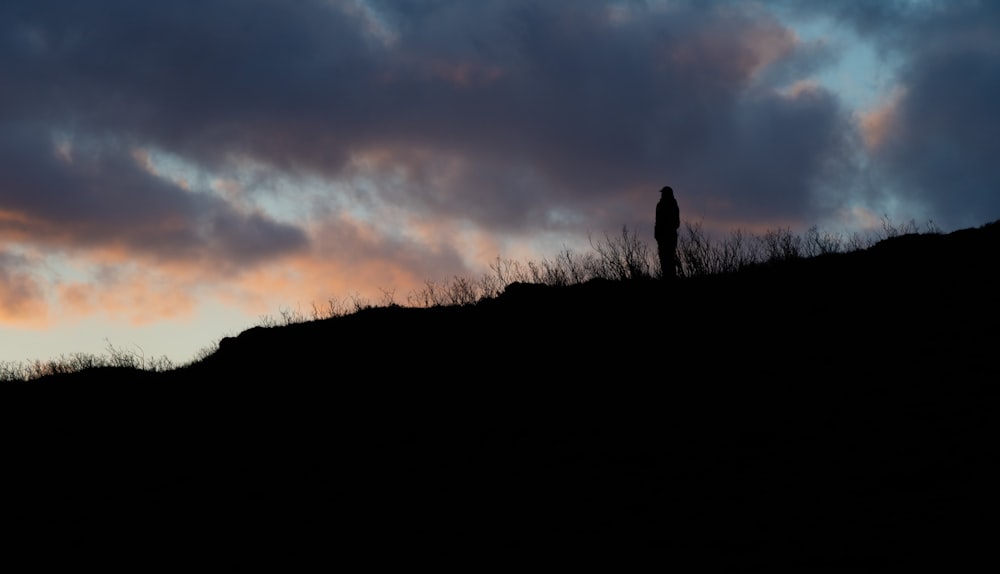 a person standing on top of a hill under a cloudy sky