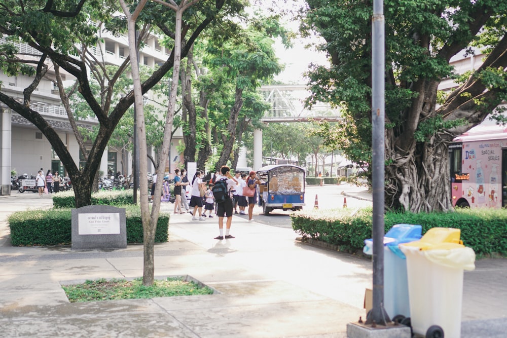 a group of people walking down a sidewalk next to trees