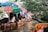 A group of people seated in wooden boats with colorful umbrellas, navigating a narrow canal surrounded by lush greenery and trees.