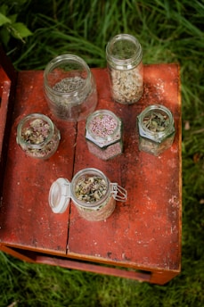 Small glass jars filled with colorful dried herbs arranged on a wooden table.
