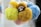 A collection of fluffy keychains with various colors and a small doll's face visible among them. The items have bright, soft textures and are arranged closely together, creating a cozy and whimsical appearance.