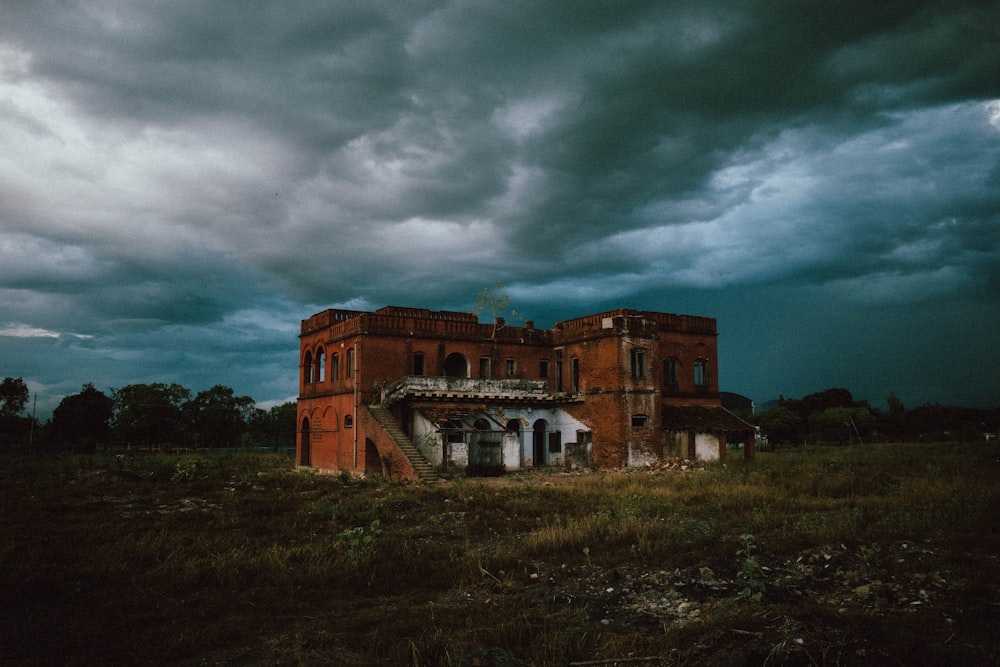 an abandoned building in a field under a cloudy sky
