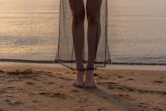 A serene outdoor scene with Lilith walking barefoot on warm sand at sunset.