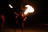 A dazzling fire dancer performing with flames against a dark elegant event backdrop.