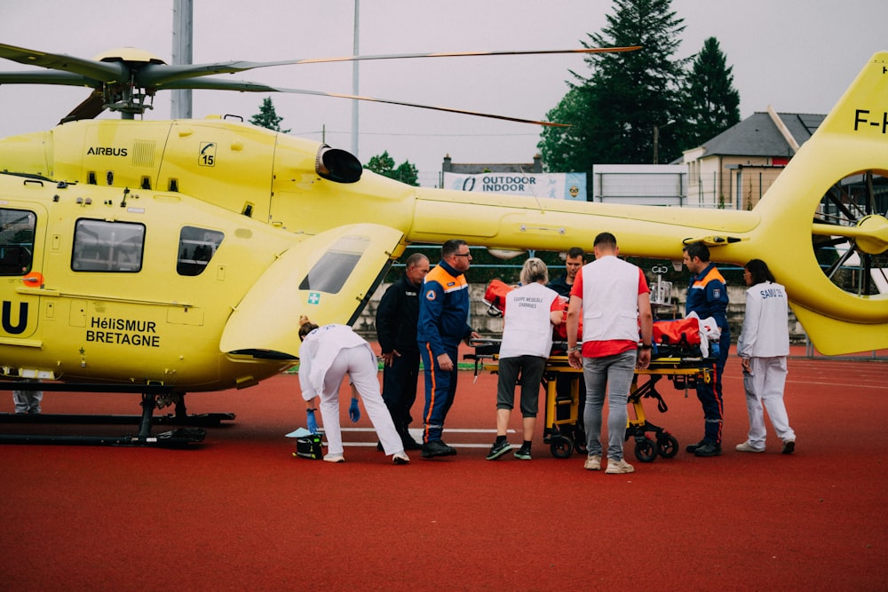 a group of people standing around a yellow helicopter