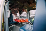 The interior of an emergency vehicle is equipped with medical apparatus, seats, and a stretcher. Various medical equipment and monitors are mounted on the walls, and the space is designed for quick access and functionality.