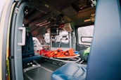 The interior of an emergency vehicle is equipped with medical apparatus, seats, and a stretcher. Various medical equipment and monitors are mounted on the walls, and the space is designed for quick access and functionality.
