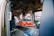 The interior of an emergency vehicle is equipped with medical apparatus, seats, and a stretcher. Various medical equipment and monitors are mounted on the walls, and the space is designed for quick access and functionality.