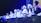 A group of individuals wearing traditional attire and head coverings appear to be engaged in a panel discussion or ceremony. They are seated at a table with various items like bottles of water and fruits in front of them. The setting is dimly lit with blue and yellow stage lights highlighting the participants.