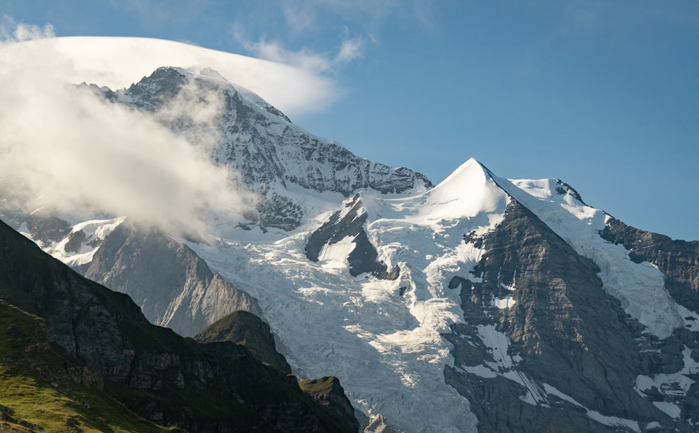 a mountain covered in snow and clouds under a blue sky