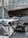 A luxurious indoor setting with a geometric glass ceiling and reflective marble floor. Three high-end luxury cars, including a black and white color scheme, are prominently displayed. A red velvet rope separates the cars from the viewer, suggesting exclusivity.