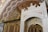 An ornate, decorative interior featuring intricate patterns and luxurious design. The ceiling and walls are adorned with detailed floral and geometric motifs in rich, warm tones. The structure includes lavish gold embellishments and a grand white marble archway with intricate carvings.