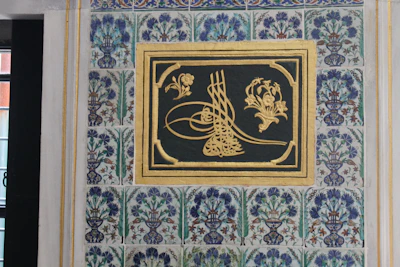 Intricately designed calligraphy art piece framed in warm beige and gold tones.