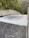 A powerful flow of water is cascading down a smooth, wide concrete structure, likely a dam spillway. Surrounding the spillway are lush green trees and dense forested hills.