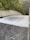 A powerful flow of water is cascading down a smooth, wide concrete structure, likely a dam spillway. Surrounding the spillway are lush green trees and dense forested hills.