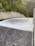 A powerful flow of water is cascading down a smooth, wide concrete structure, likely a dam spillway. Surrounding the spillway are lush green trees and dense forested hills.