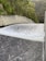 A powerful flow of water is cascading down a smooth, wide concrete structure, likely a dam spillway. Surrounding the spillway are lush green trees and dense forested hills.