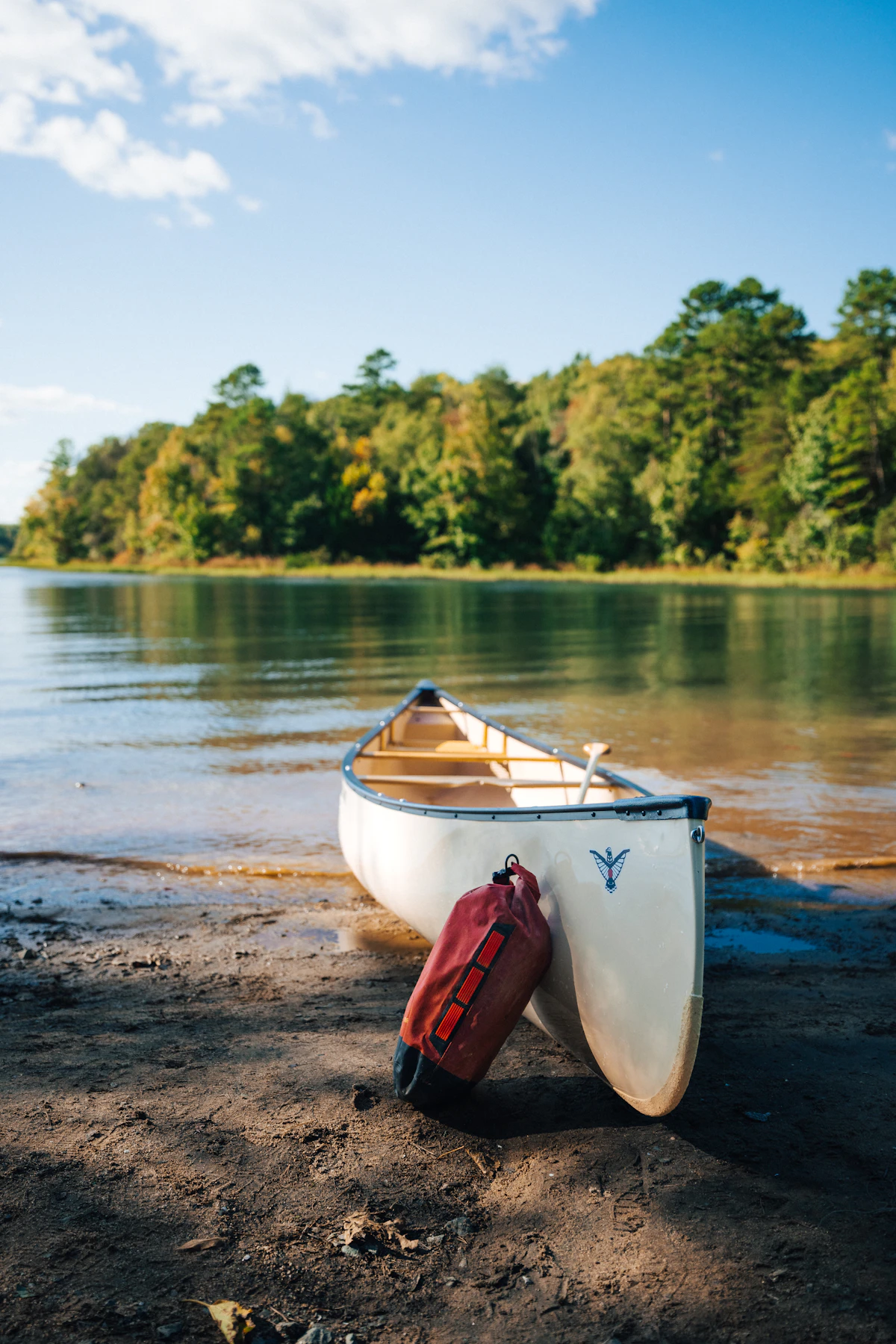 Red roll-top dry bag leaning against a canoe on a lakeshore