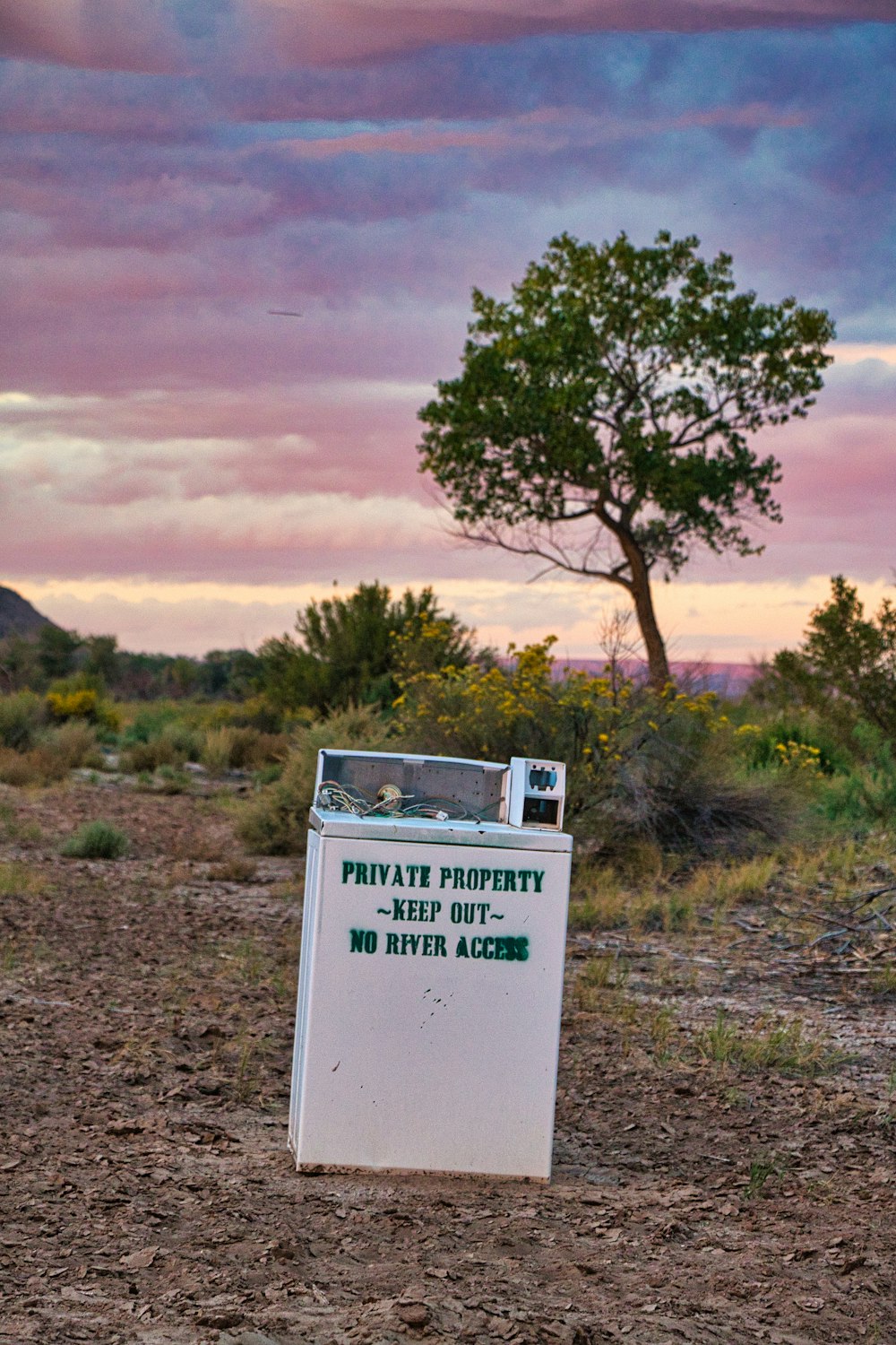 Un cartello in mezzo a un campo con un albero sullo sfondo
