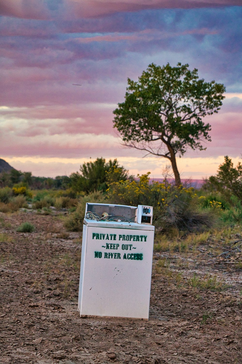 a sign in the middle of a field with a tree in the background