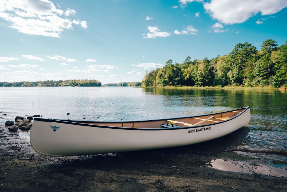 a white canoe sitting on the shore of a lake