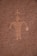 A rock surface features an ancient petroglyph depicting a humanoid figure with outstretched arms. The carving is etched into a textured reddish-brown rock face, typical of prehistoric rock art.