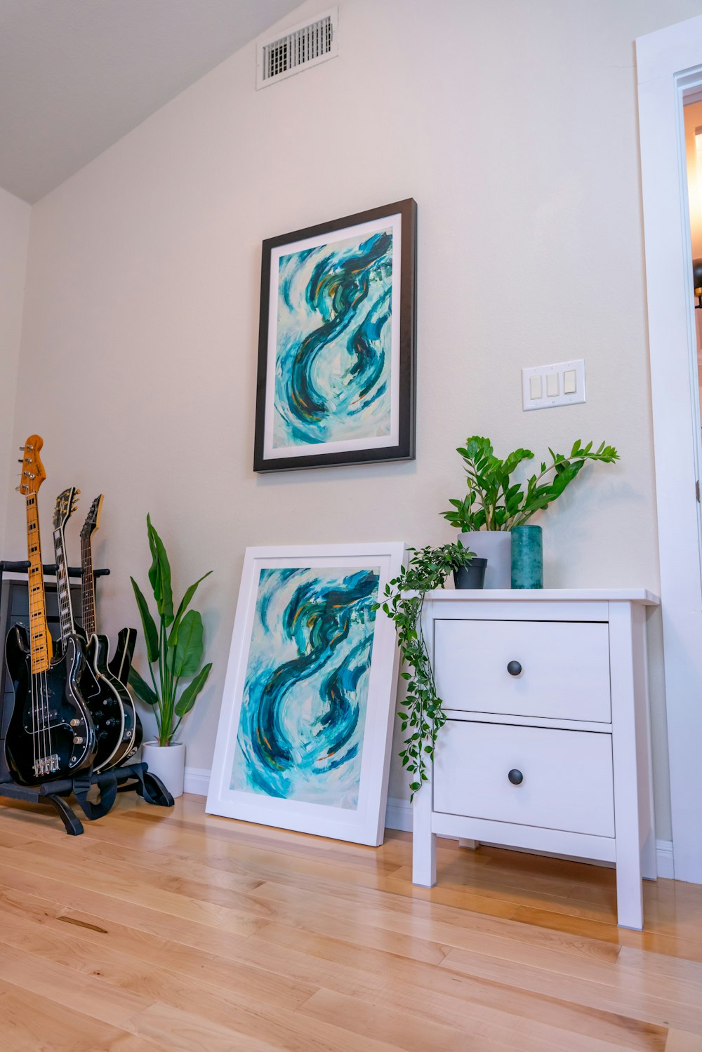 a room with a guitar, plant, and picture on the wall