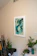 A softly lit corner of a living room featuring a framed abstract artwork with deep forest green and muted clay tones.