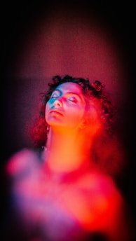 A person with curly hair and closed eyes appears surrounded by vibrant red and blue light effects, creating a surreal and dreamy atmosphere.