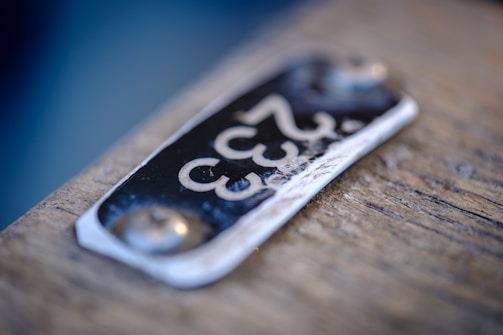 A close-up of a metal plate with the number '333' embossed on it, attached to a wooden surface. The plate appears slightly worn with visible scratches and two rivets securing it to the surface.